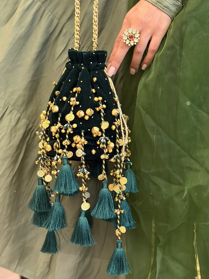 A green velvet drawstring potli bag decorated with gold coins, ghungroos, and tassels. Hand-embellished potli bag.